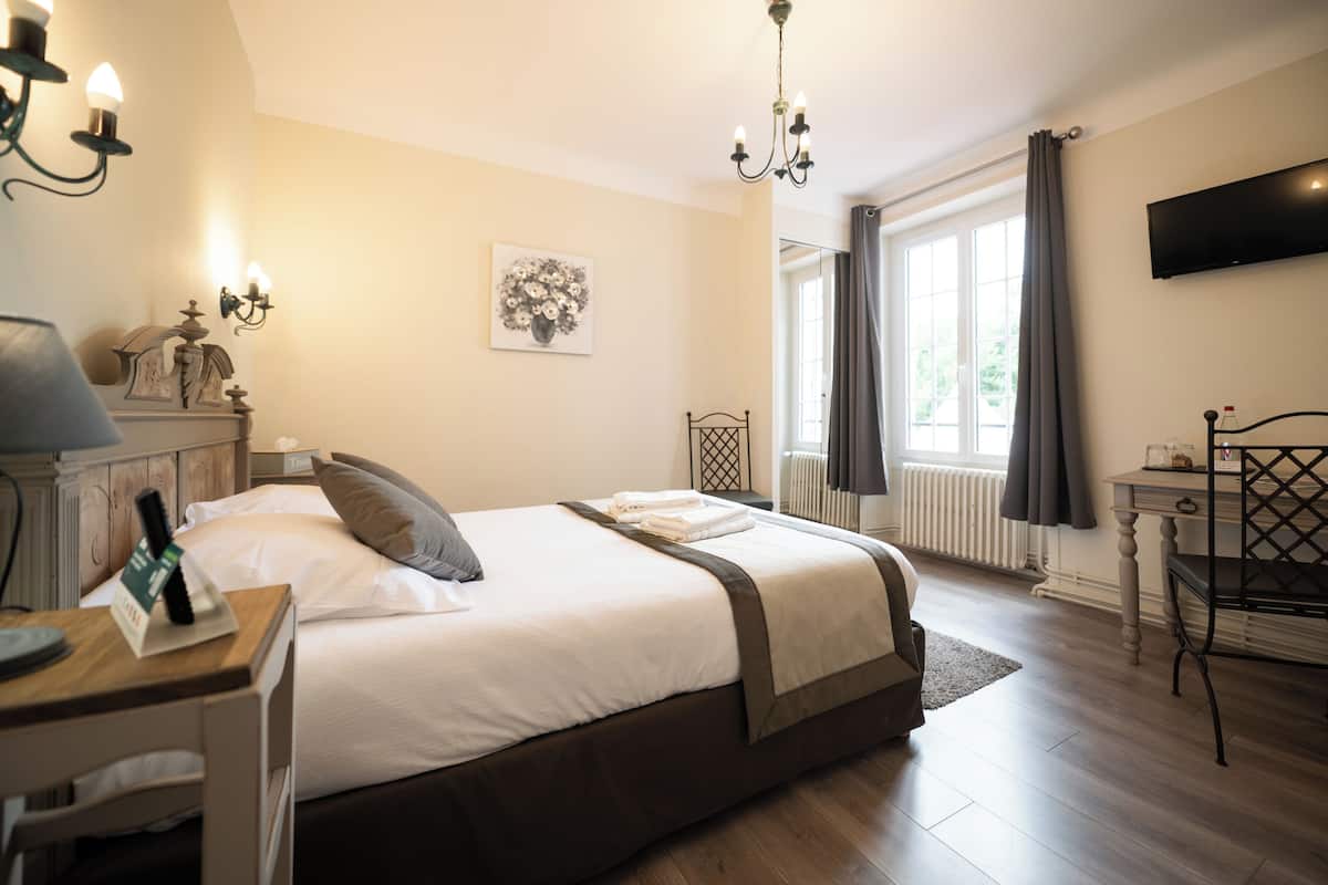A hotel room with a bed, bedside table, lamp, artwork, and a TV.