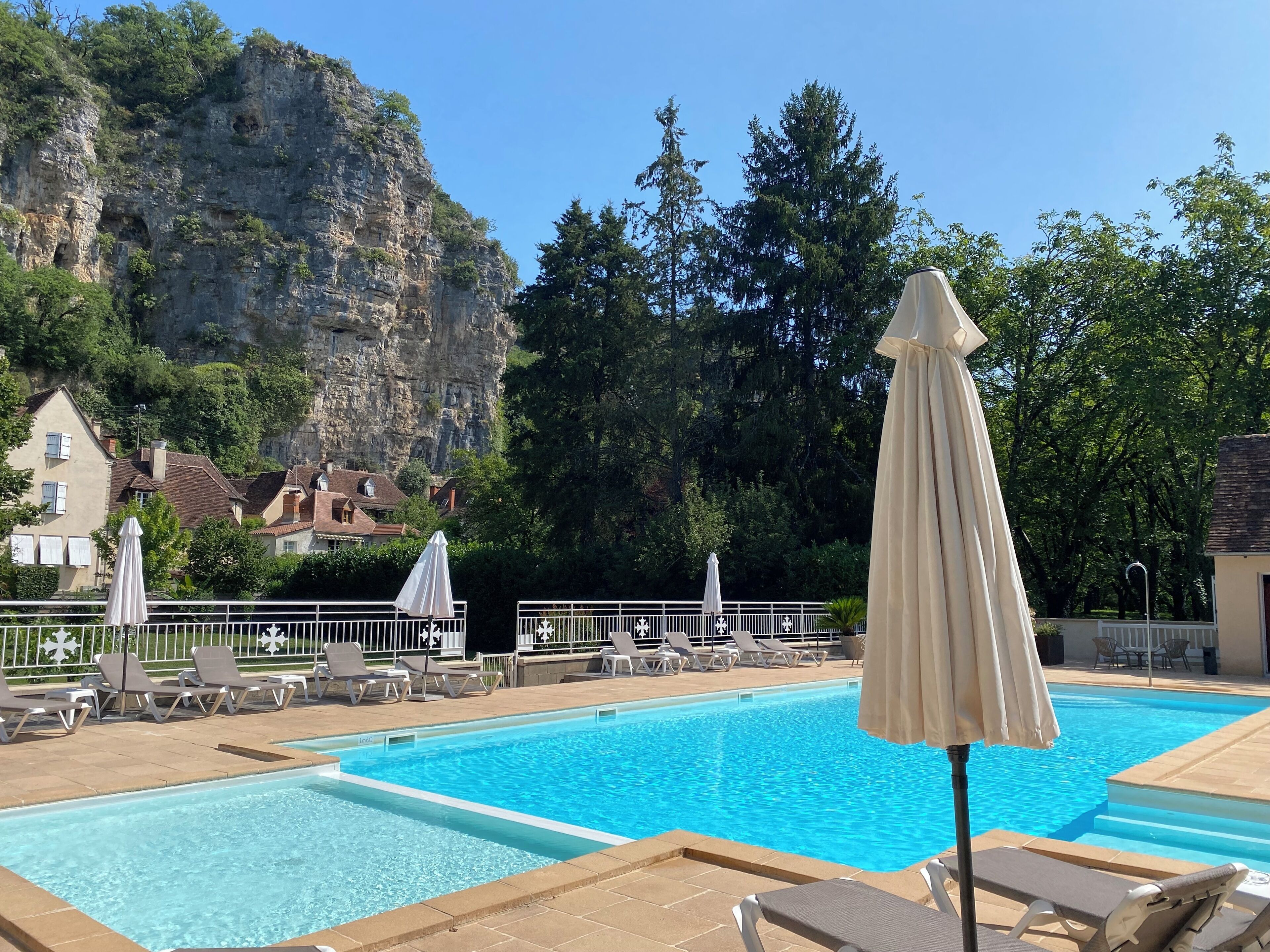 Une piscine entourée de chaises longues et de parasols, le tout niché au cœur d’un paysage montagneux et bordé d’arbres.