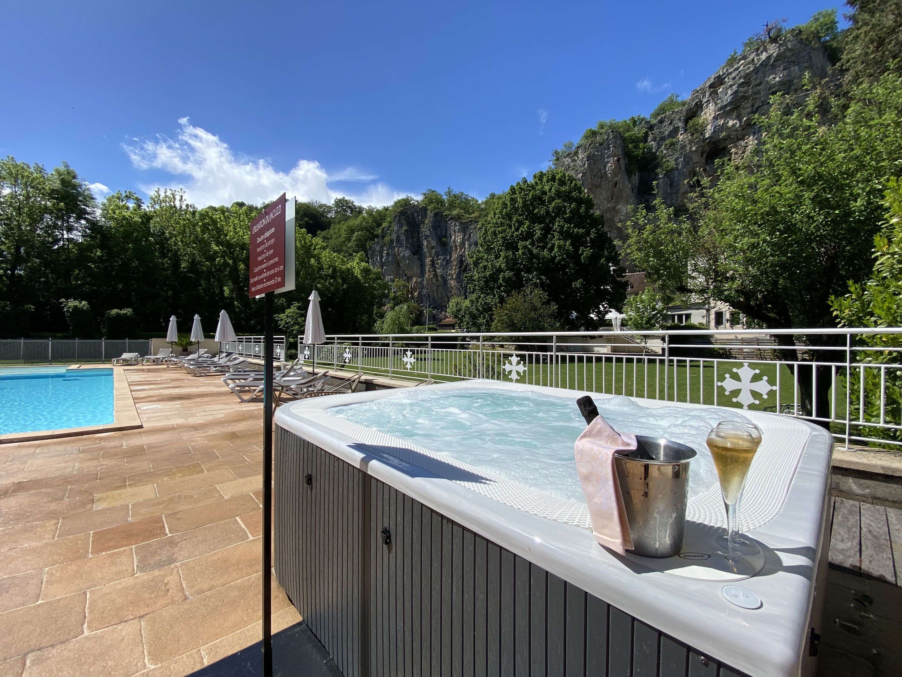 Un bain à remous avec une boisson et une bouteille, entouré de chaises longues et d’une piscine.
