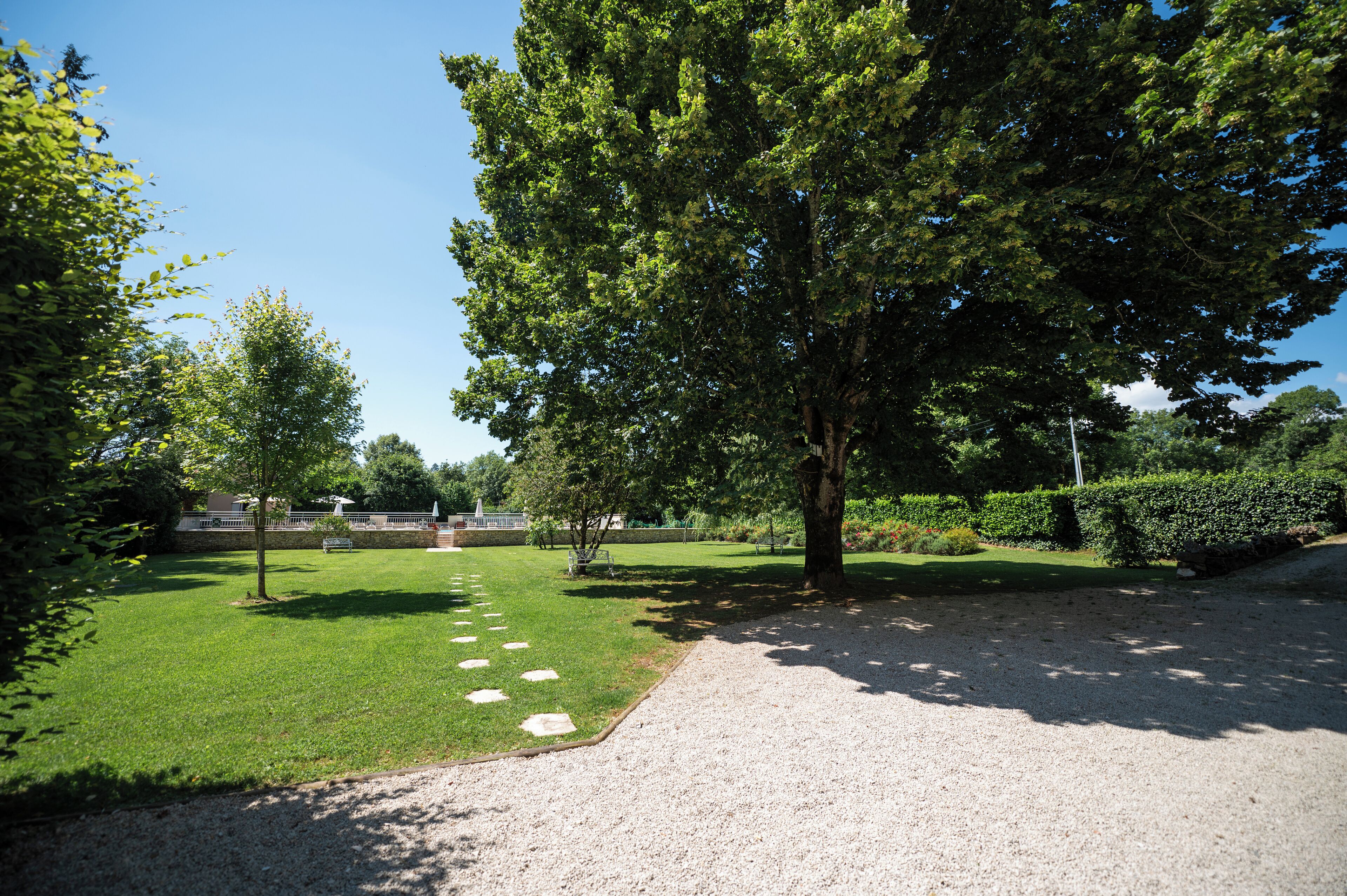 A well-maintained garden with a gravel path, neatly trimmed grass, and a variety of trees.