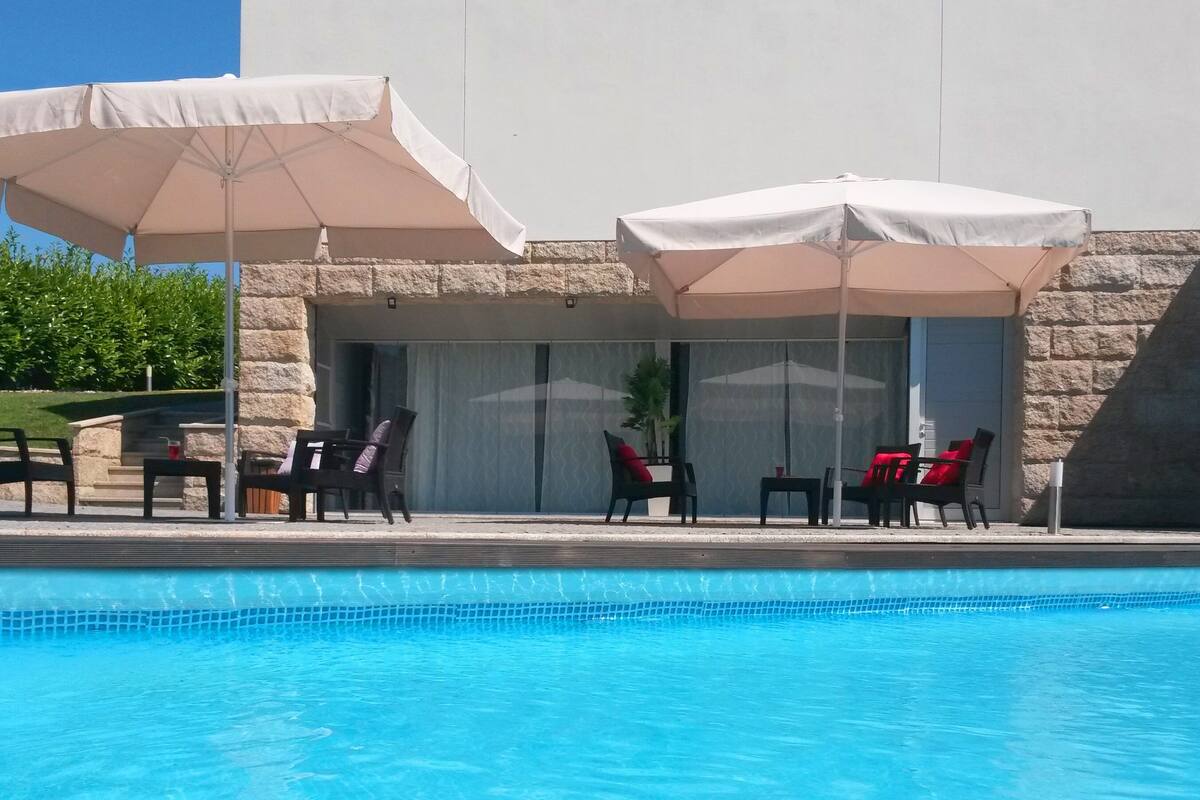 A pool area with lounge chairs and umbrellas, a stone wall, and a door with a sliding glass window.