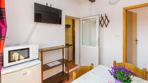 Een kleine kamer met een magnetron, een televisie, een houten stoel, een tafel met een vaas met paarse bloemen, en een deur naar een andere kamer.