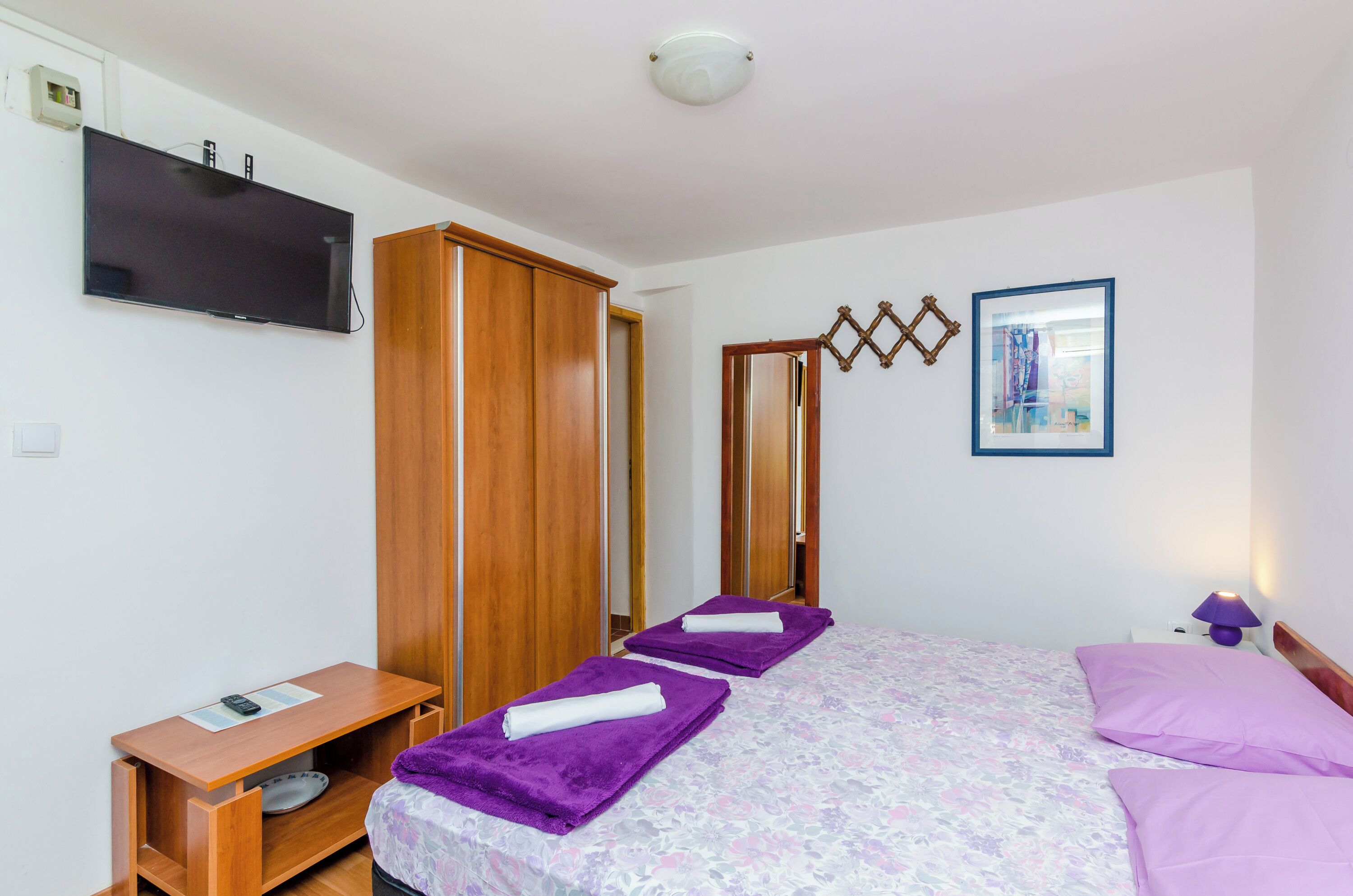 A hotel room with a bed, a TV, a wardrobe, and a bedside table.