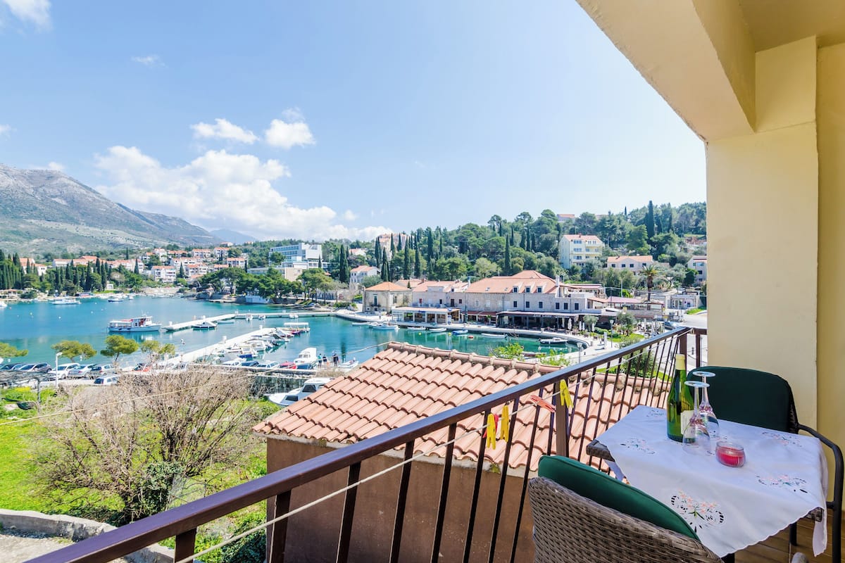 Un balcon avec une table, des chaises et une vue sur un port de plaisance et des immeubles.