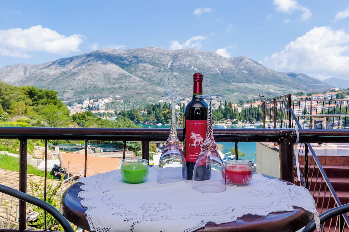 Une table avec une bouteille de vin, deux verres et deux boissons sur un balcon donnant sur un paysage montagneux.