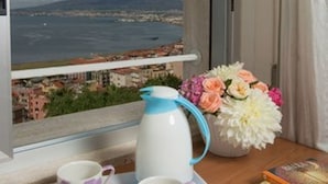 Una stanza con vista su una città costiera, un tavolo con teiera, tazze e un vaso di fiori.