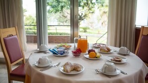 Una tavola imbandita per la colazione, con piatti, tazze e una brocca di succo d'arancia, affacciata su un giardino.