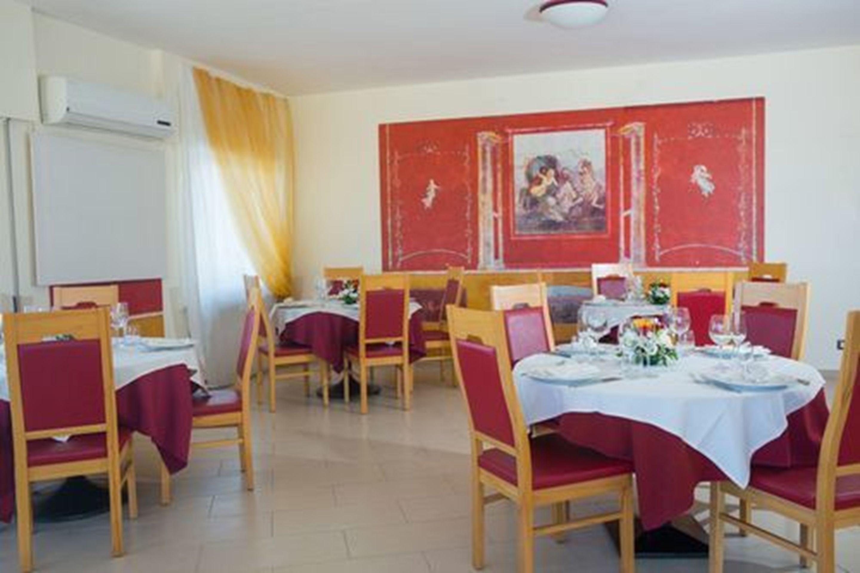 A dining area with tables set for four, red chairs, and a red wall with a framed picture.