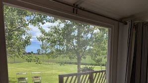 A room with a large window overlooking a grassy area with a wooden deck and chairs. - Corte Galvana (Cento)