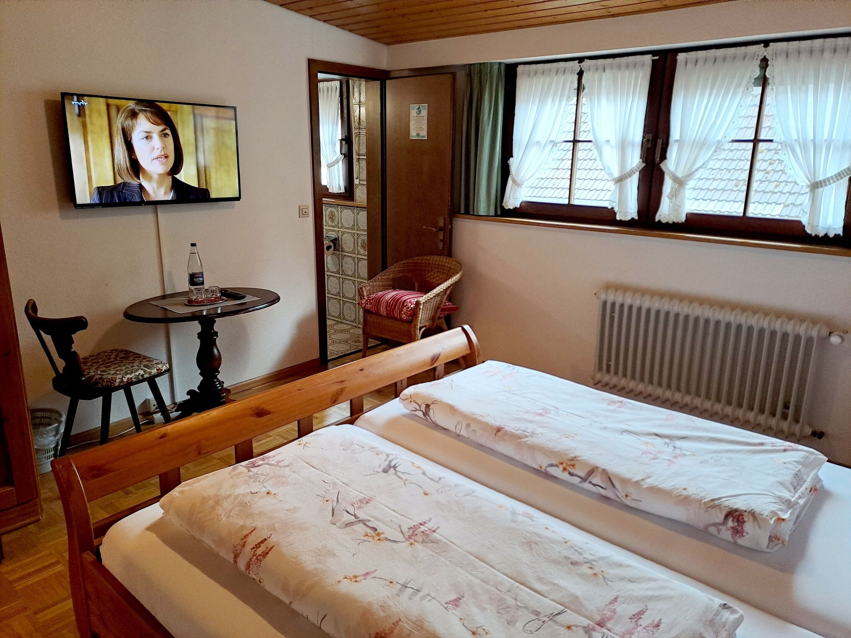 Une chambre avec deux lits, une table sur laquelle se trouve une bouteille, une chaise et un téléviseur fixé au mur.