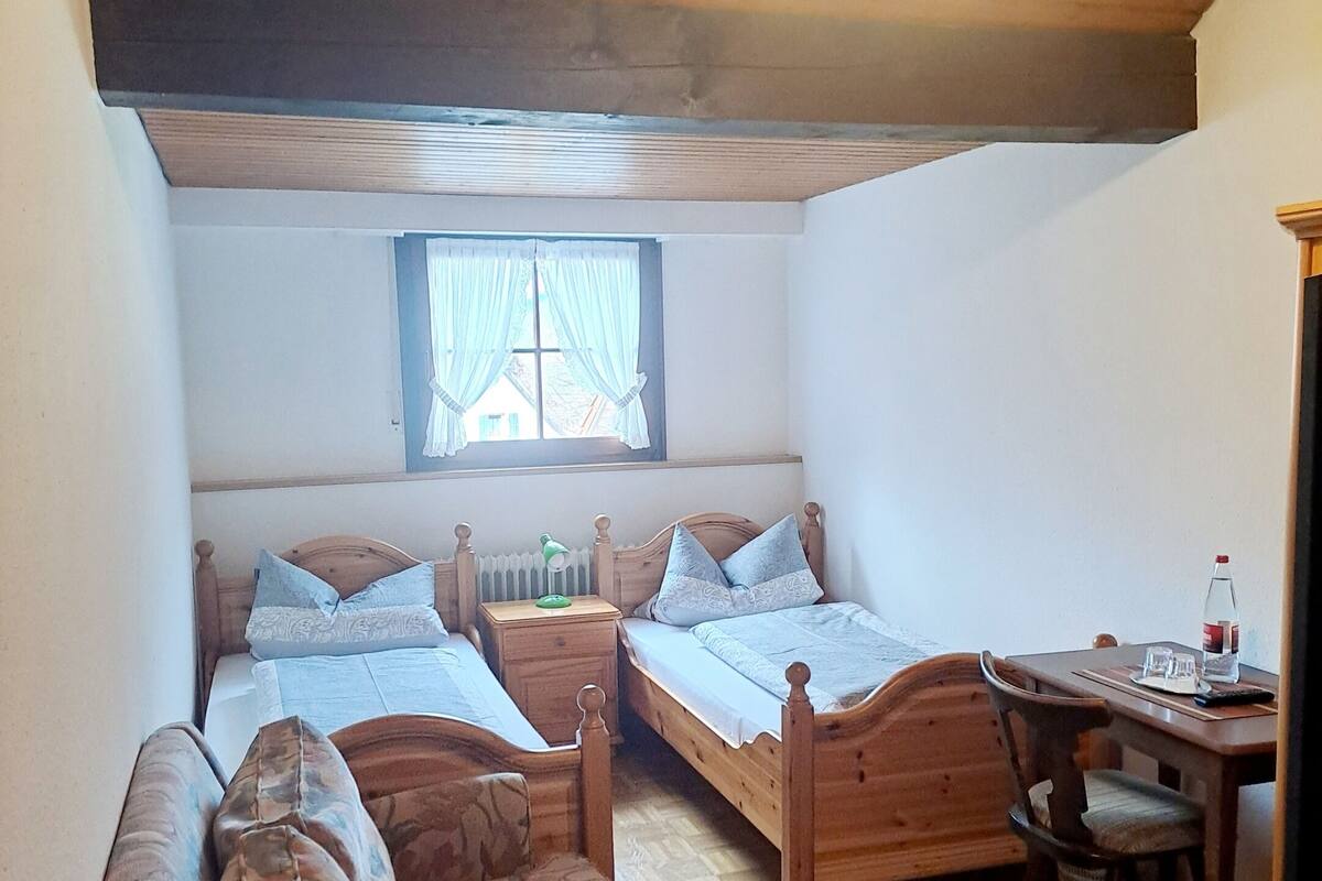 A cozy attic bedroom with two wooden beds, a small table, and a chair.