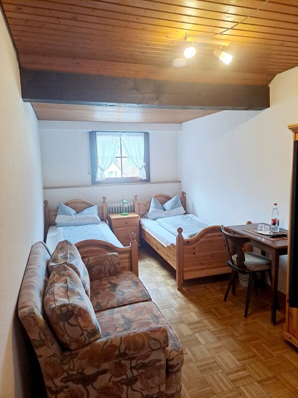 A cozy attic bedroom with two wooden beds, a small table, and a chair. - Pension Schlossbergblick (Simonswald)