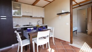 A kitchen with white cabinets, a dining table with blue bowls, and white chairs. - Villaggio Residence Torre Saracena - Campsite (Camerota)