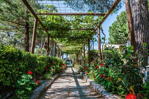 Un sentier bordé de verdure et de fleurs rouges, qui mène à une structure en forme de pergola.