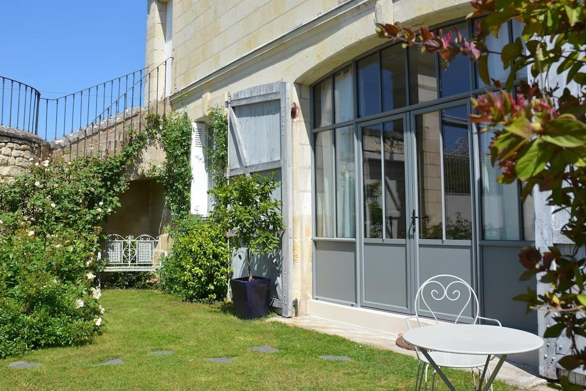 A building with a stone facade, large windows, and a small garden with a bench and a table.