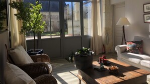 A living room with a large window, wicker furniture, a wooden coffee table, and a potted plant. - La Pénesais (Beaumont-en-Veron)