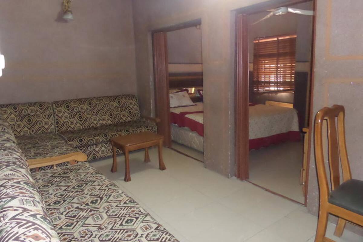 A room with a patterned sofa, a small wooden table, and a mirror reflecting a bed with a red blanket.