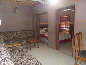Una habitación con un sofá estampado, una pequeña mesa de madera y un espejo que refleja una cama con una manta roja.