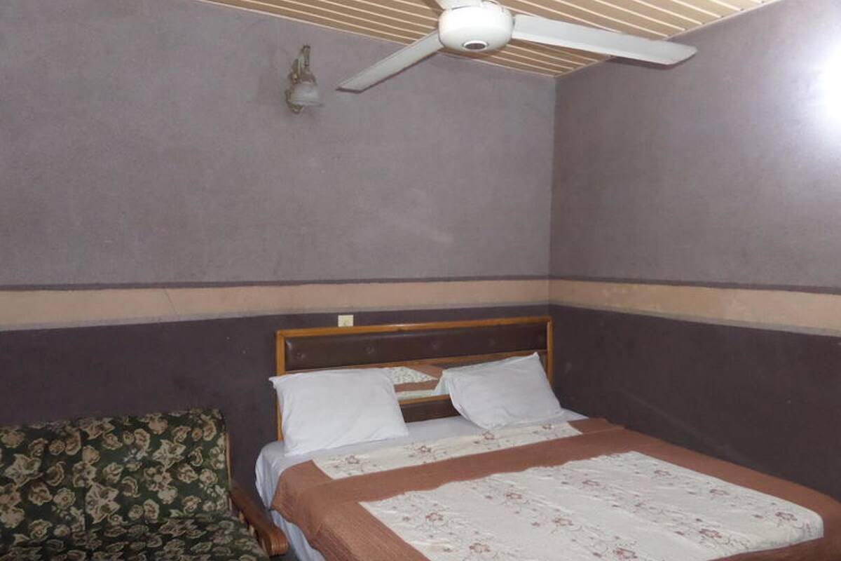 A bedroom with a bed, a ceiling fan, and a patterned chair.