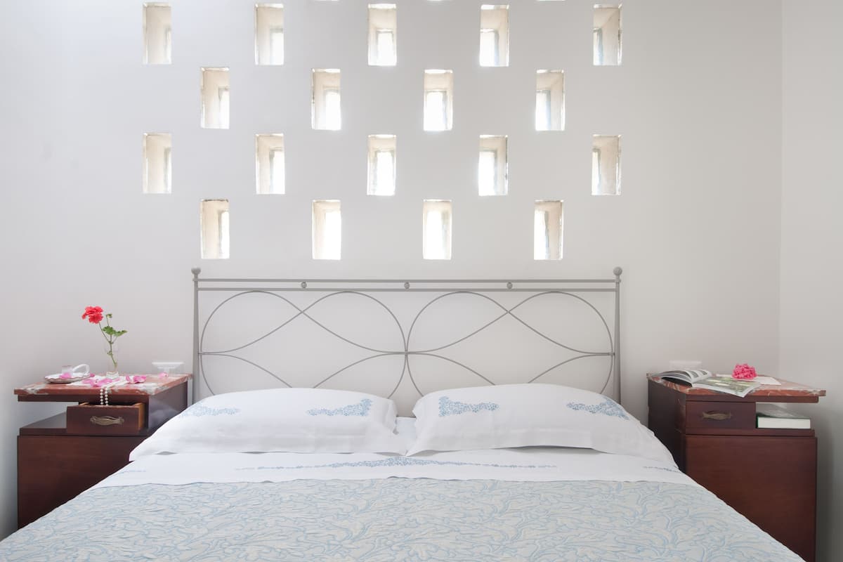 Ein Schlafzimmer mit einem Bett, zwei Nachttischen, einer Kommode und einer Wand mit mehreren kleinen Fenstern.