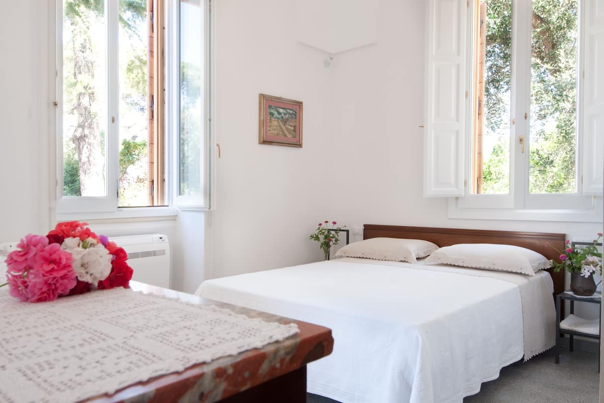Ein Schlafzimmer mit einem großen Bett, einem kleineren Bett, einem Schreibtisch mit Blumen in einer Vase und einem gerahmten Bild an der Wand.