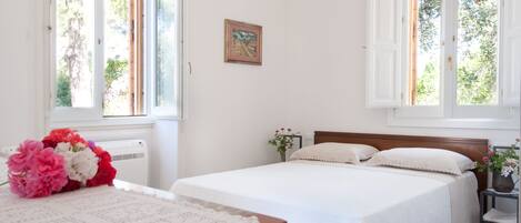 A bedroom with a large bed, a smaller bed, a desk with a vase of flowers, and a framed picture on the wall.