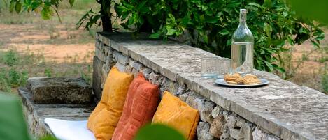 A stone bench with orange cushions, a bottle, and biscuits.