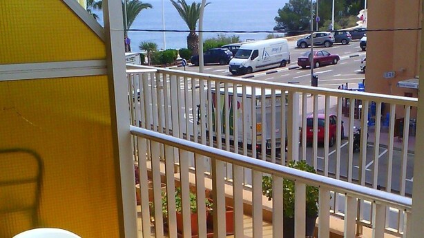 A balcony with white chairs and a small round table, overlooking a street with parked cars and palm trees. - Pensión el Hidalgo (Calpe)