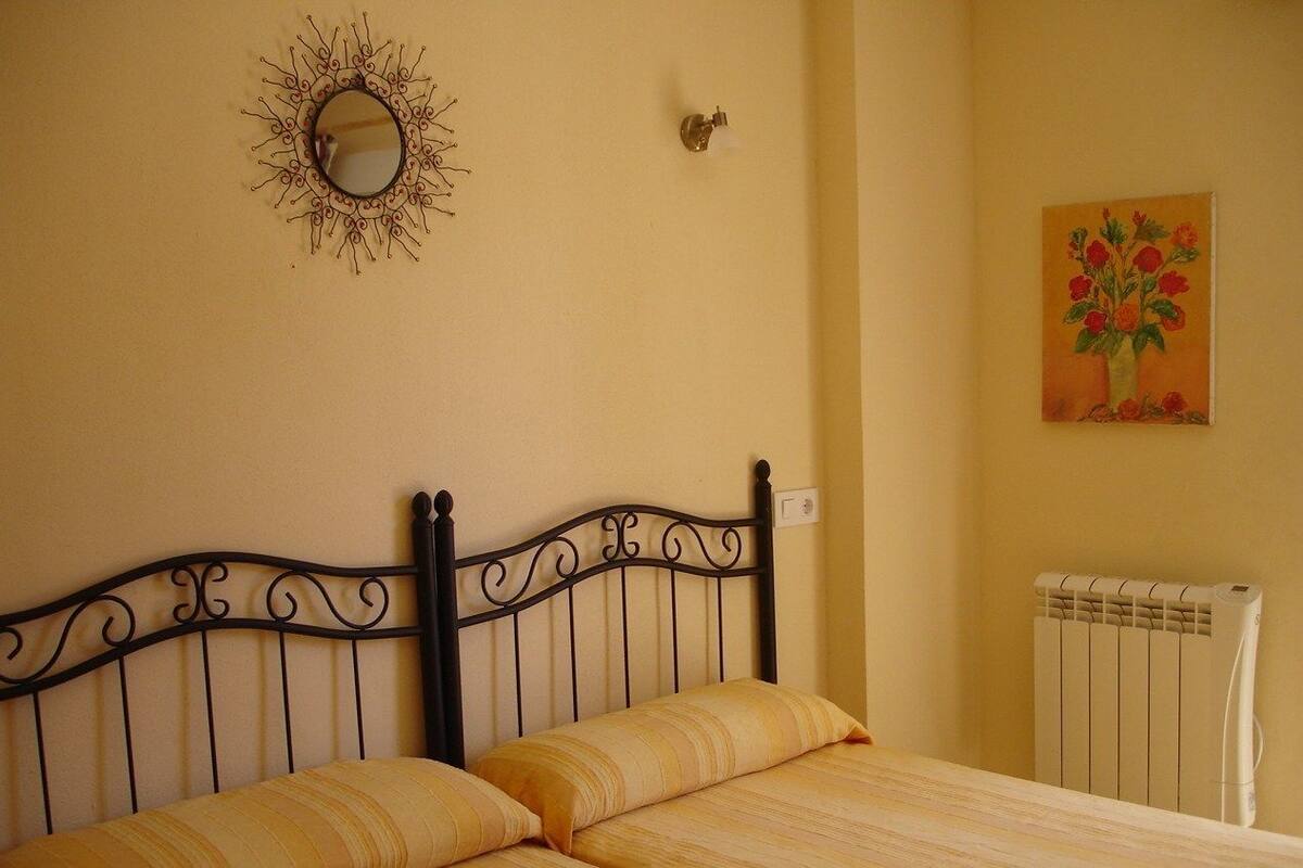 A bed with a metal headboard, a wall-mounted mirror, a radiator, and a painting of flowers.