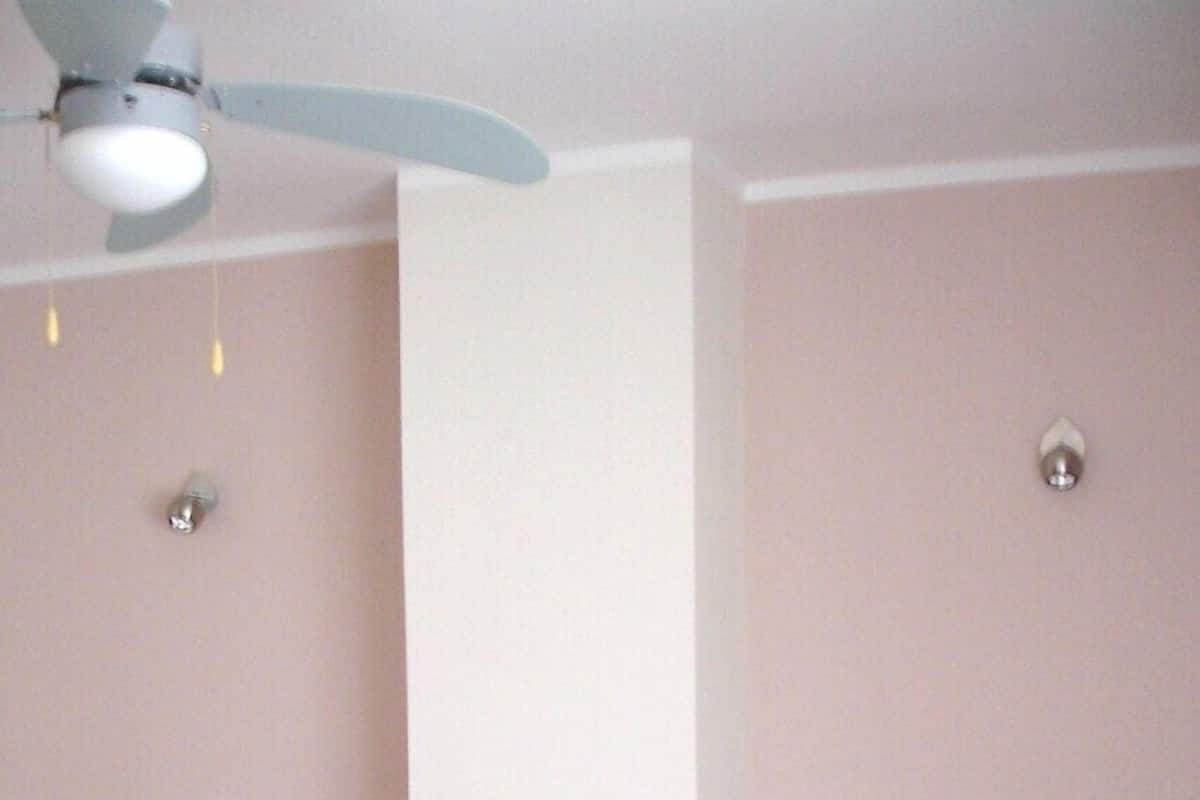 A bedroom with two single beds, a wooden nightstand, a ceiling fan, and a wall socket.