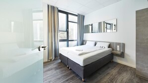 Une chambre à coucher moderne, dotée d’un grand lit, d’une table de chevet, d’un miroir et offrant une vue sur l’extérieur grâce à de grandes fenêtres.