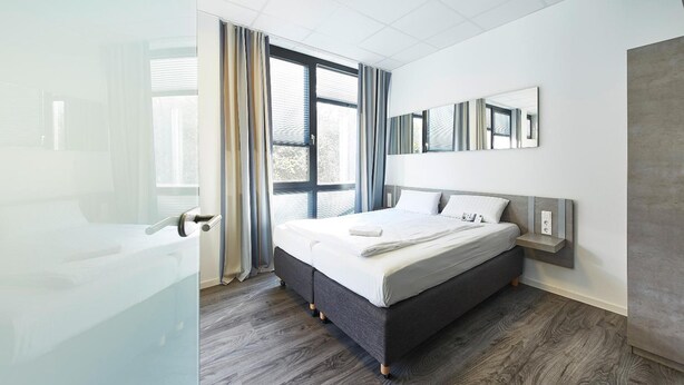 Un dormitorio moderno con una cama grande, una mesita de noche, un espejo y vistas al exterior a través de amplios ventanales.