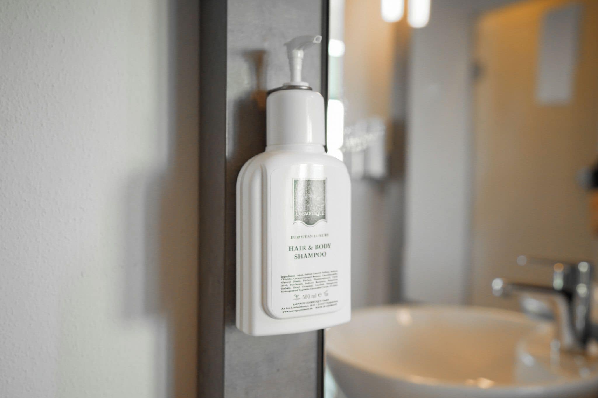 Un baño con una botella blanca de champú y gel de ducha en un dispensador de pared.