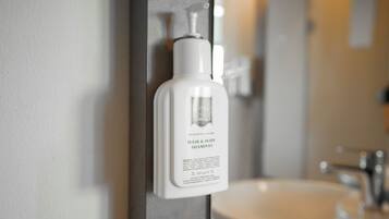 Un baño con una botella blanca de champú y gel de ducha en un dispensador de pared.