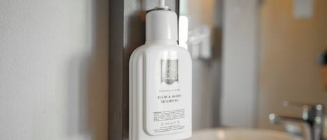 A bathroom with a white bottle of hair and body shampoo on a wall-mounted dispenser.