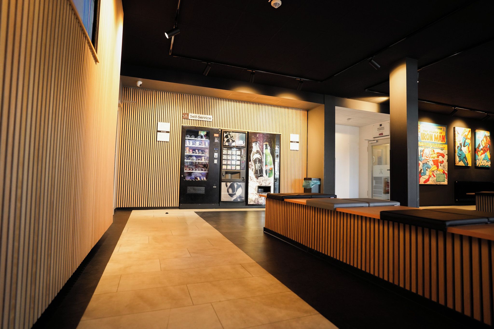 A modern reception area with a wooden reception desk, a self-service kiosk, and a wall with comic book posters.