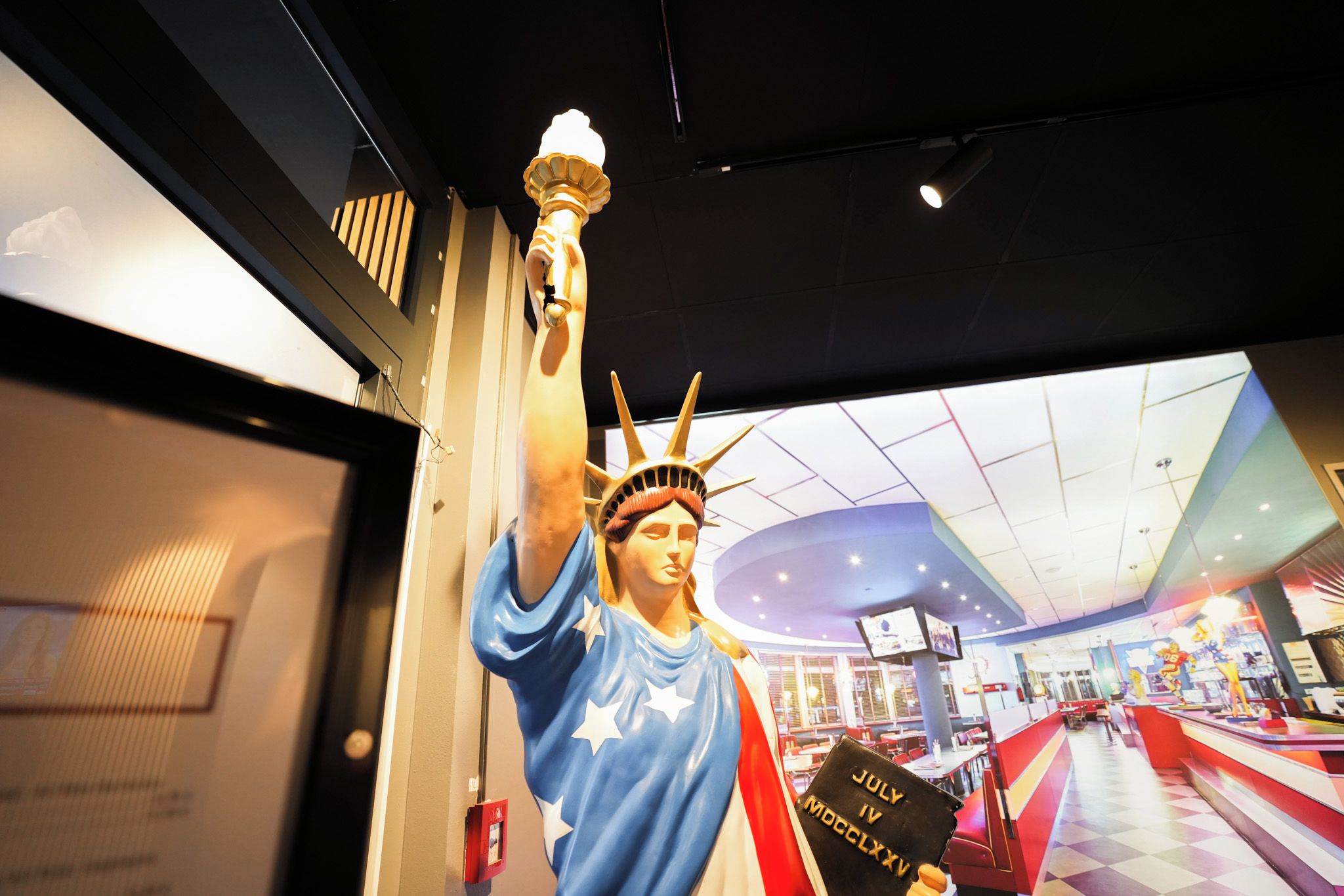 Une statue de la Statue de la Liberté tenant une torche, avec une pancarte indiquant « 4 JUILLET » et « 4 JUILLET 2020 » au premier plan.