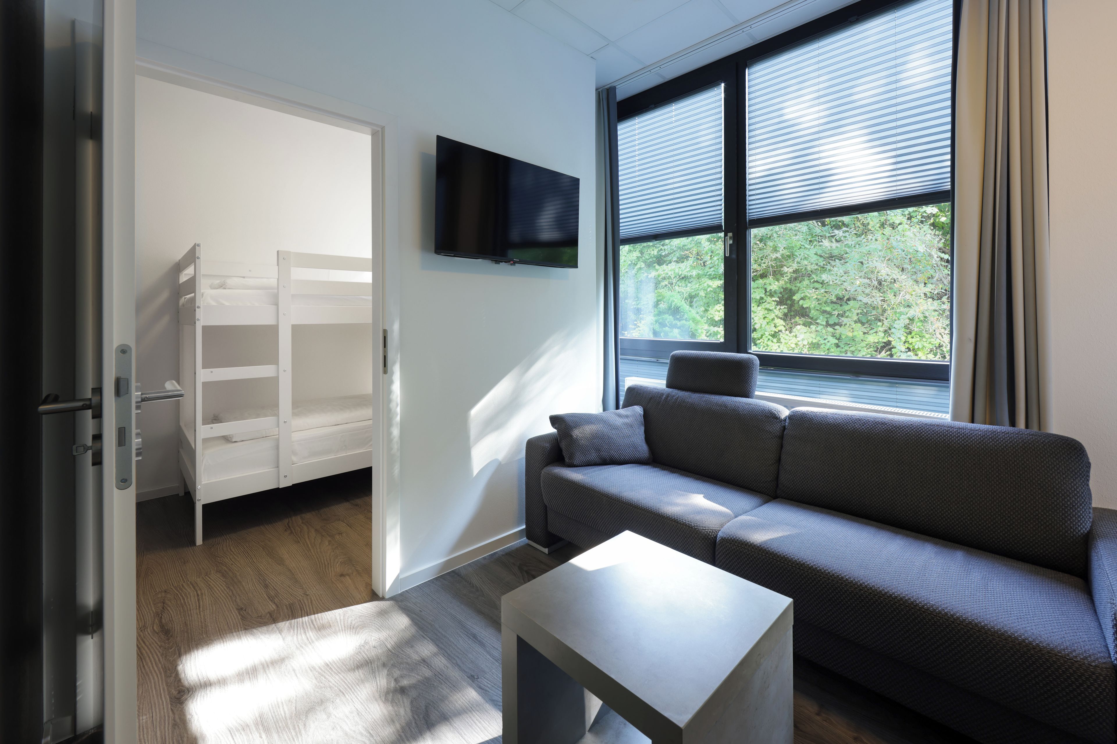 Ein modernes Zimmer mit einem grauen Sofa, einem kleinen weißen Tisch und einem an der Wand montierten Fernseher.