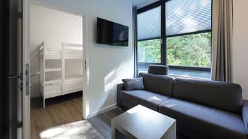 Ein modernes Zimmer mit einem grauen Sofa, einem kleinen weißen Tisch und einem an der Wand montierten Fernseher.