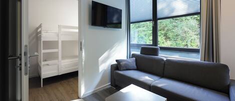 Una habitación moderna con un sofá gris, una mesita blanca y un televisor montado en la pared.