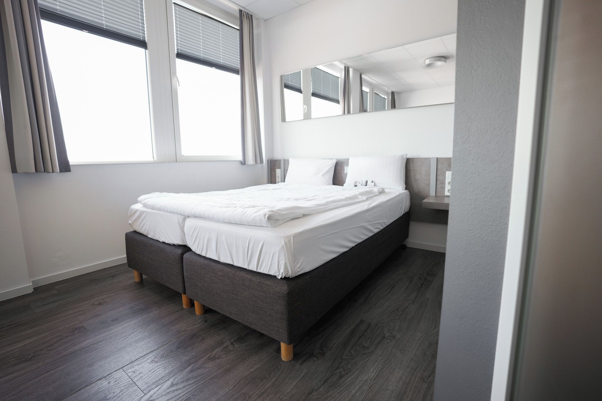 Une chambre moderne avec un lit, une table de chevet et une grande fenêtre équipée de stores.