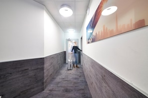 A narrow hallway with a wooden floor, white walls, and a cityscape mural. - Road House Hotel (Paderborn)