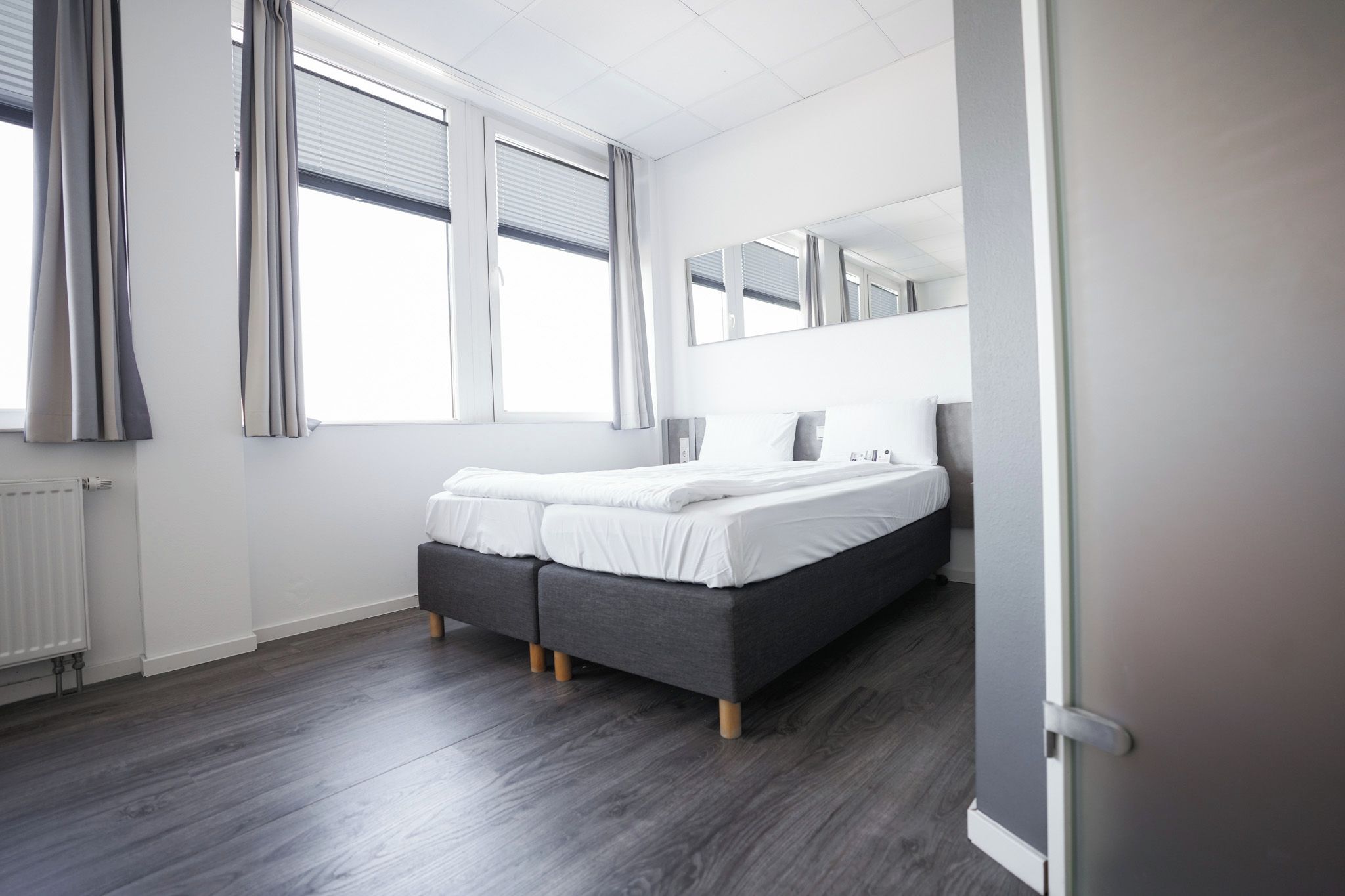 Una camera da letto con un letto matrimoniale, una testiera imbottita grigia e un grande specchio sopra il letto.