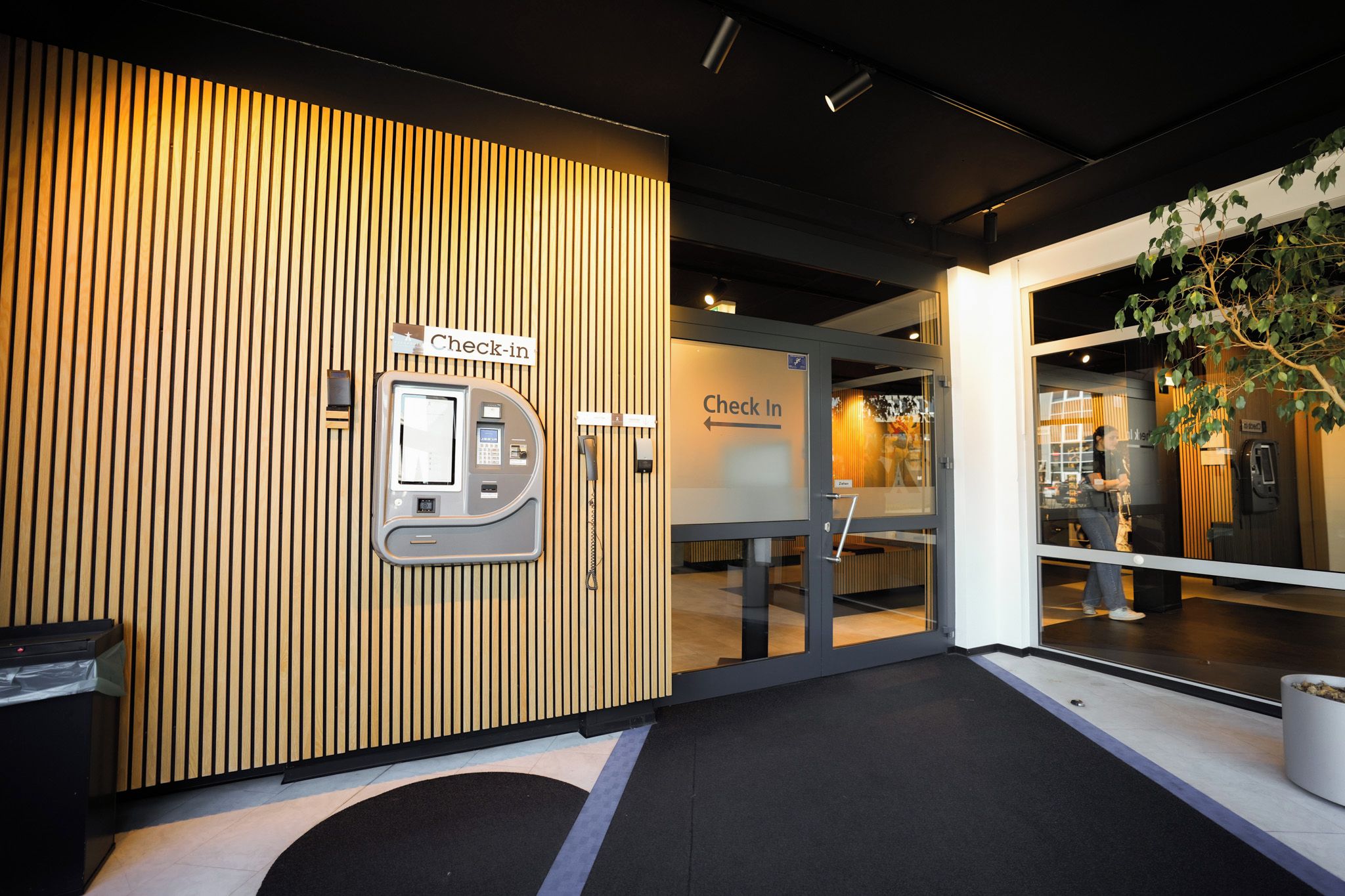 A check-in area with a wooden panel wall, a reception desk, and a glass door leading inside.