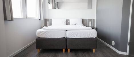 Un dormitorio moderno con cama doble, cabecero gris y un espejo grande encima.