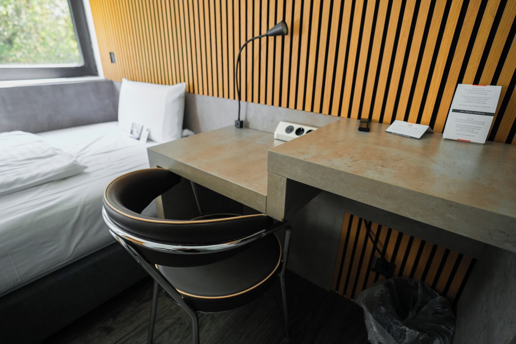 A modern hotel room with a bed, a desk, a chair, and a lamp.