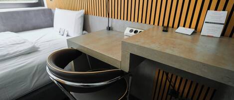 A modern hotel room with a bed, a desk, a chair, and a lamp.