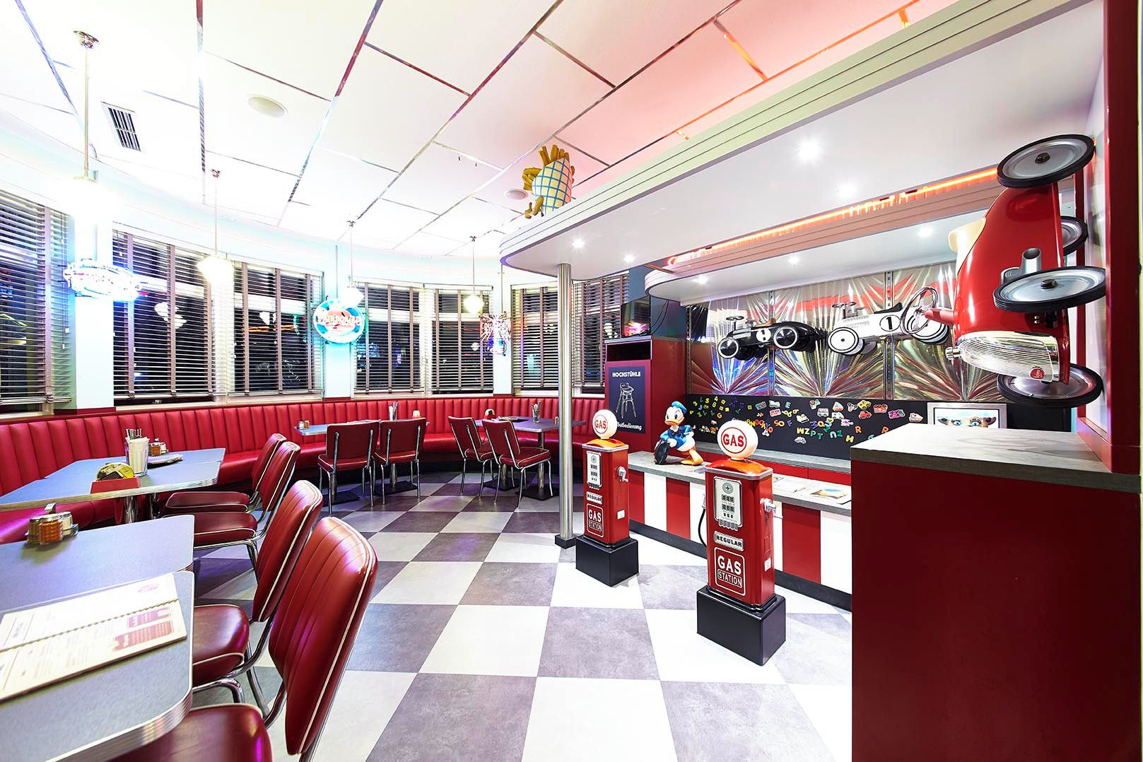 A diner with red booths and tables, a jukebox, and a neon sign.