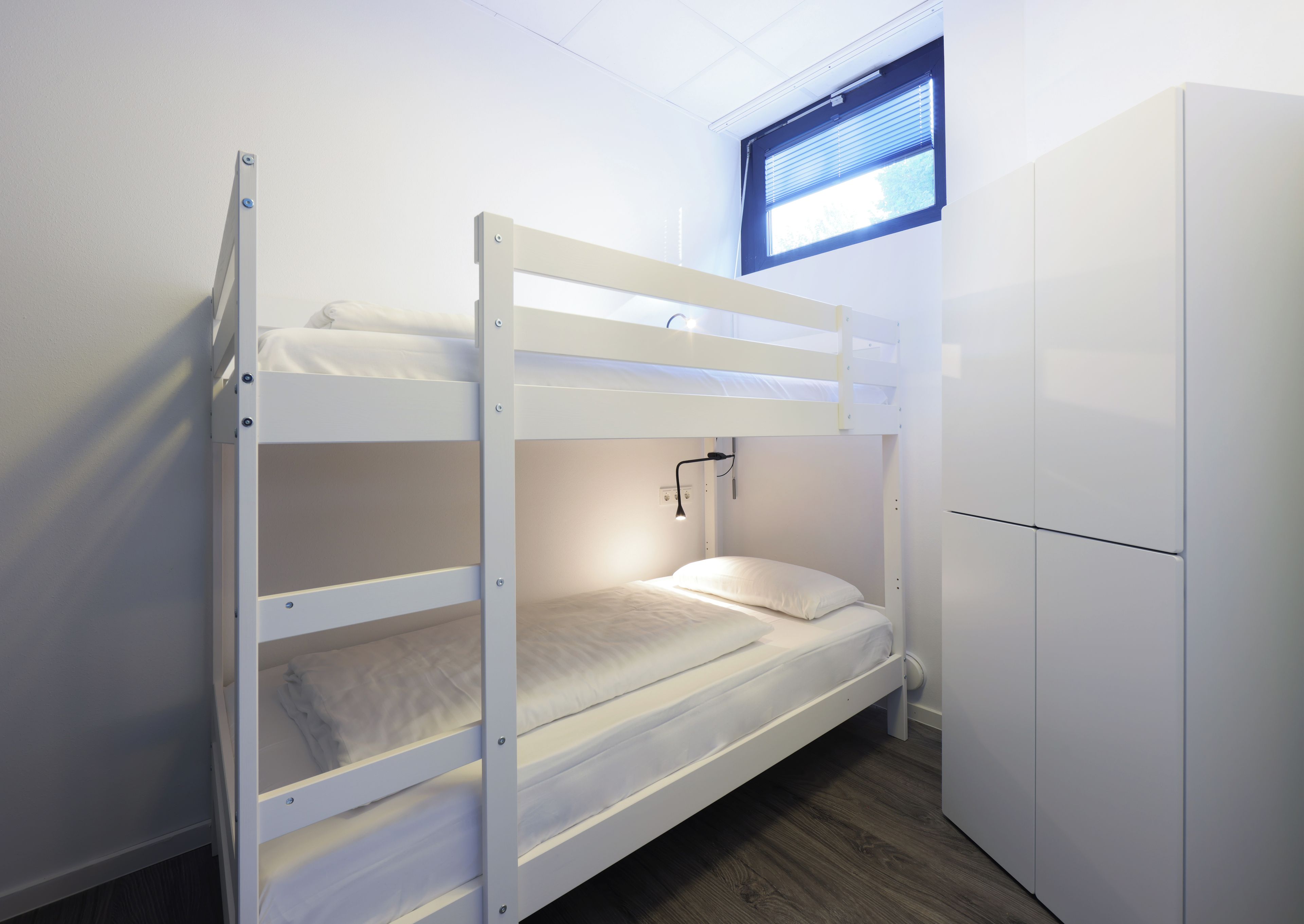 A bunk bed with a desk and a window, all in white.