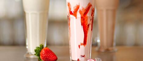 Tres batidos con crema batida y una fresa, servidos en vasos de vidrio transparente con pajitas a rayas.